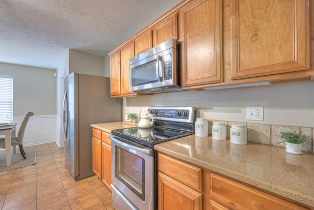 5451 Middlebury Dr, Murfreesboro, TN 37128 - kitchen with appliances with stainless steel finishes, light tile patterned floors, a textured ceiling, brown cabinets, and a wainscoted wall