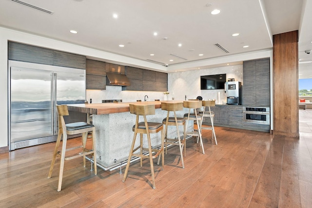 1212 Laurel St Unit 1510, Nashville, TN 37203 - kitchen featuring appliances with stainless steel finishes, wall chimney range hood, modern cabinets, light wood-type flooring, and a kitchen bar