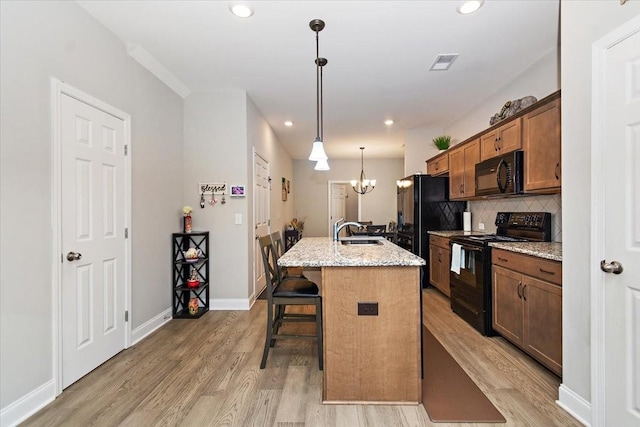433 Longstone Rd, Gallatin, TN 37066 - kitchen with black appliances, light wood-style floors, a kitchen island with sink, a breakfast bar area, and tasteful backsplash