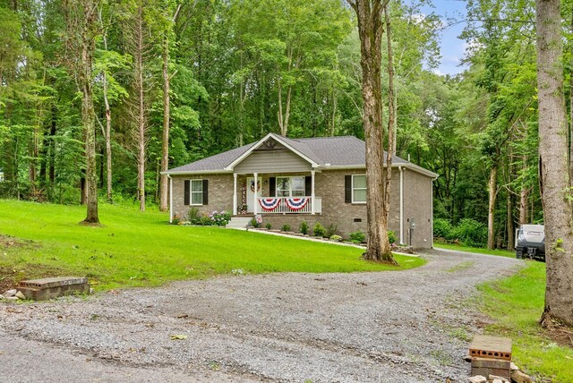 516 Cedarcrest Dr, Chapmansboro, TN 37035 - single story home with a porch, a front yard, a wooded view, gravel driveway, and brick siding