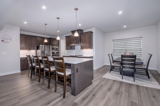 1401 Kennebec Dr, Smyrna, TN 37167 - kitchen with appliances with stainless steel finishes, light wood-type flooring, an island with sink, tasteful backsplash, and dark brown cabinetry