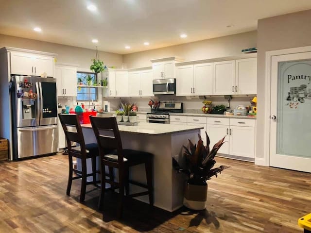1241 Emerson Cir, Hopkinsville, KY 42240 - kitchen with appliances with stainless steel finishes, white cabinetry, a kitchen island, wood finished floors, and a breakfast bar