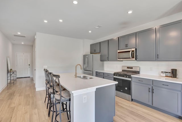 120 Millbrook Dr, Spring Hill, TN 37174 - kitchen featuring stainless steel appliances, gray cabinets, a kitchen island with sink, a kitchen bar, and light wood-style flooring