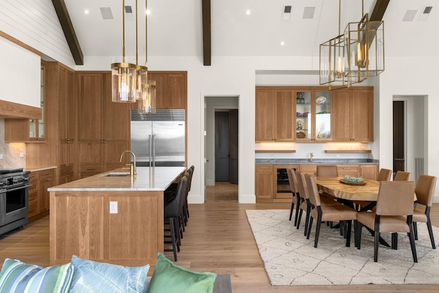 7346 Harlow Dr, College Grove, TN 37046 - kitchen featuring stainless steel appliances, wine cooler, brown cabinetry, beam ceiling, and light wood-style flooring