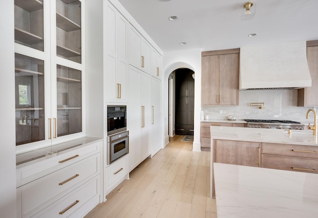 1713 Reflection Ln, Brentwood, TN 37027 - kitchen featuring arched walkways, premium range hood, stainless steel gas stovetop, light stone countertops, and light wood-type flooring