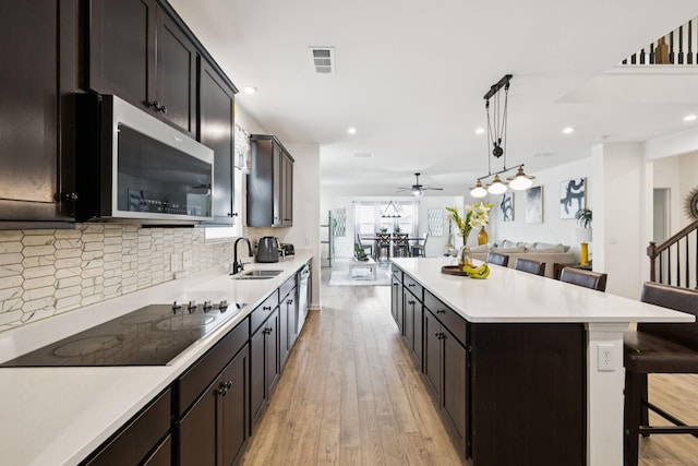 809 Old Blue Ln, Murfreesboro, TN 37130 - kitchen with black electric stovetop, stainless steel microwave, open floor plan, a kitchen breakfast bar, and light wood-style flooring