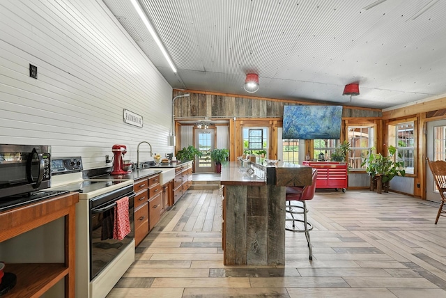 1880 Clydeton Rd, Waverly, TN 37185 - kitchen with white electric stove, wood walls, stainless steel microwave, a breakfast bar area, and light wood-type flooring
