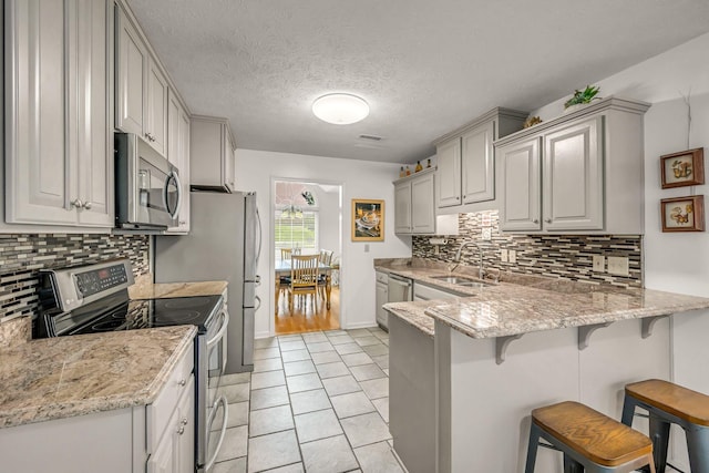 1013 Laurel Hills Dr, Dickson, TN 37055 - kitchen with stainless steel appliances, a peninsula, a breakfast bar, backsplash, and gray cabinetry