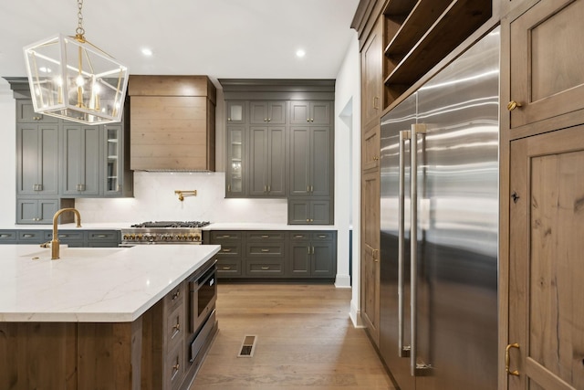 6628 Bethesda Arno Rd, Thompsons Station, TN 37179 - kitchen with built in appliances, exhaust hood, a chandelier, light wood finished floors, and light stone counters