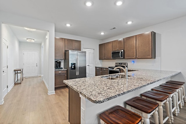 832 Green Meadow Ln, Smyrna, TN 37167 - kitchen with appliances with stainless steel finishes, a peninsula, a kitchen breakfast bar, light stone counters, and light wood-type flooring