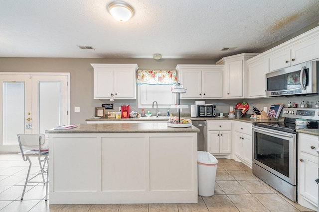 982 Chesire Way, Gallatin, TN 37066 - kitchen with stainless steel appliances, a kitchen island, white cabinetry, light tile patterned floors, and a textured ceiling