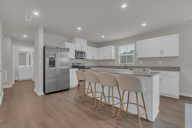 1830 Quail Run Way, Spring Hill, TN 37174 - kitchen with appliances with stainless steel finishes, a kitchen island, a breakfast bar, white cabinetry, and light wood-style floors
