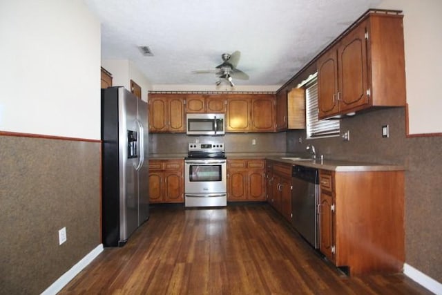 1211 Patton Pl, Oak Grove, KY 42262 - kitchen featuring appliances with stainless steel finishes, dark wood-style flooring, brown cabinets, a ceiling fan, and a wainscoted wall
