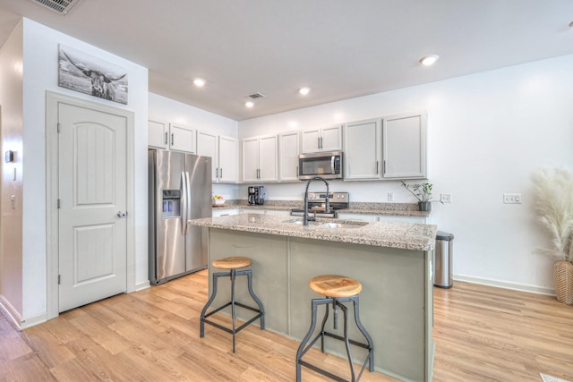 3105 Defilade Dr, Murfreesboro, TN 37128 - kitchen with appliances with stainless steel finishes, light wood finished floors, a kitchen breakfast bar, an island with sink, and light stone countertops