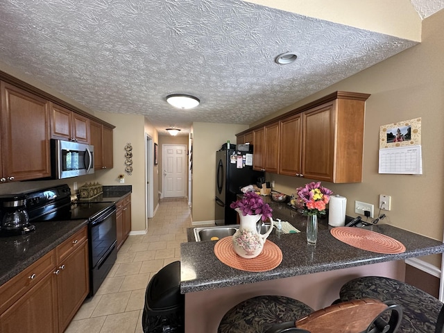 1239 Wentworth Dr, Gallatin, TN 37066 - kitchen with black appliances, light tile patterned floors, a peninsula, brown cabinetry, and a textured ceiling