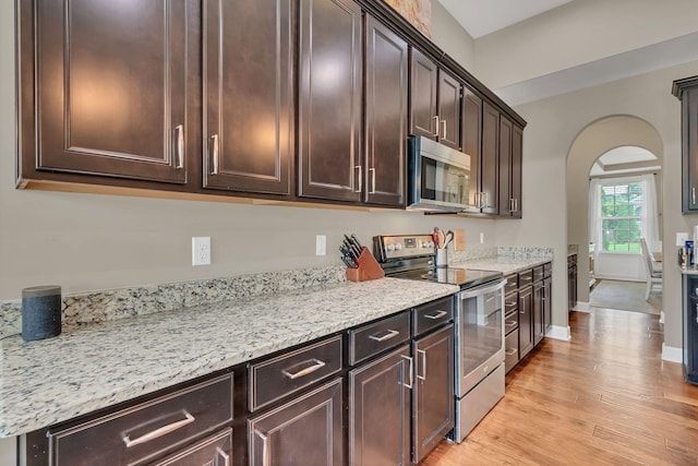 1060 Harvey Springs Dr, Spring Hill, TN 37174 - kitchen with stainless steel appliances, arched walkways, dark brown cabinetry, light wood-type flooring, and light stone countertops