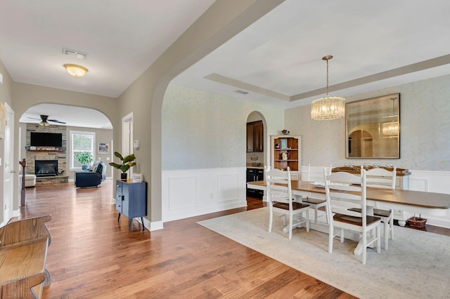 1060 Harvey Springs Dr, Spring Hill, TN 37174 - dining room featuring arched walkways, a ceiling fan, a fireplace, wood finished floors, and a wainscoted wall