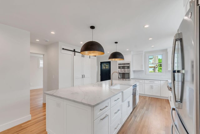 300 Natchez St, Franklin, TN 37064 - kitchen featuring stainless steel appliances, a barn door, light wood-style floors, decorative backsplash, and white cabinets