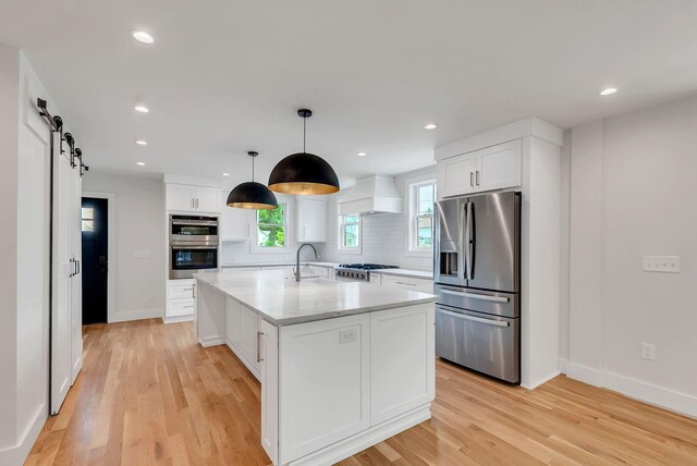 300 Natchez St, Franklin, TN 37064 - kitchen featuring appliances with stainless steel finishes, white cabinets, custom range hood, light wood finished floors, and tasteful backsplash