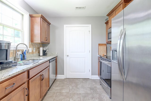 1029 Charles Thomas Dr, Clarksville, TN 37042 - kitchen featuring stainless steel appliances, brown cabinetry, light stone counters, light tile patterned floors, and decorative backsplash