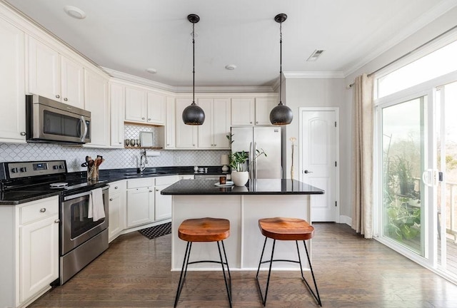 6067 Keats St, Franklin, TN 37064 - kitchen featuring appliances with stainless steel finishes, dark countertops, ornamental molding, dark wood finished floors, and a center island