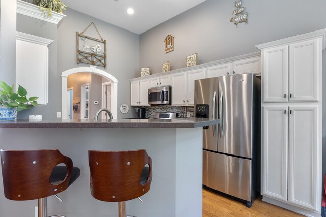 1057 Nealcrest Cir, Spring Hill, TN 37174 - kitchen featuring stainless steel appliances, white cabinetry, dark countertops, a kitchen bar, and light wood-style flooring