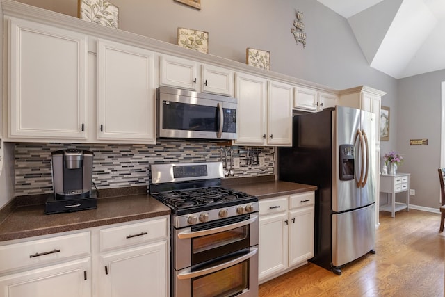 1057 Nealcrest Cir, Spring Hill, TN 37174 - kitchen featuring stainless steel appliances, vaulted ceiling, dark countertops, tasteful backsplash, and light wood-style floors