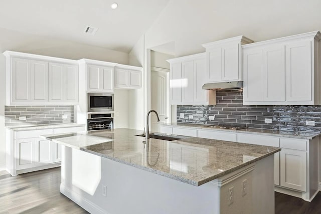 7235 Fairlawn Dr, Fairview, TN 37062 - kitchen with under cabinet range hood, decorative backsplash, a center island with sink, cooktop, and stainless steel microwave