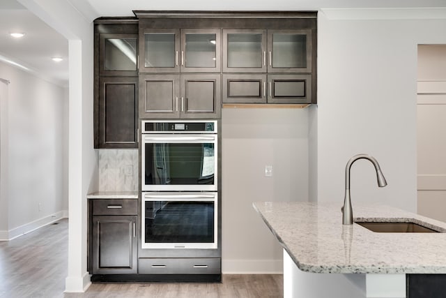 7266 Fairlawn Dr, Fairview, TN 37062 - kitchen with stainless steel double oven, light wood-type flooring, dark brown cabinets, light stone countertops, and tasteful backsplash