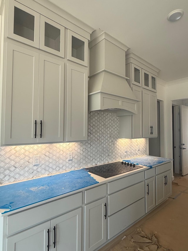 7266 Fairlawn Dr, Fairview, TN 37062 - kitchen featuring black electric stovetop, premium range hood, decorative backsplash, and glass insert cabinets