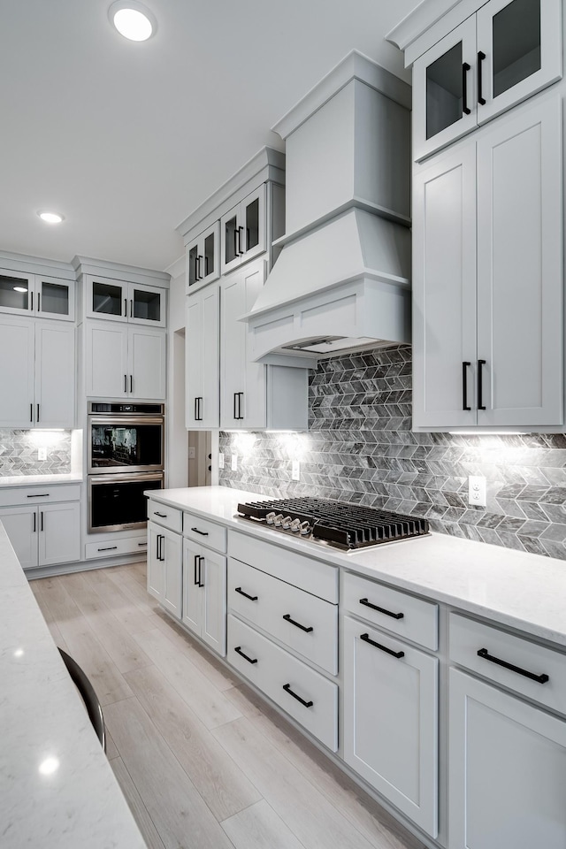 7233 Richvale Dr W, Fairview, TN 37062 - kitchen with appliances with stainless steel finishes, tasteful backsplash, light wood finished floors, premium range hood, and white cabinets