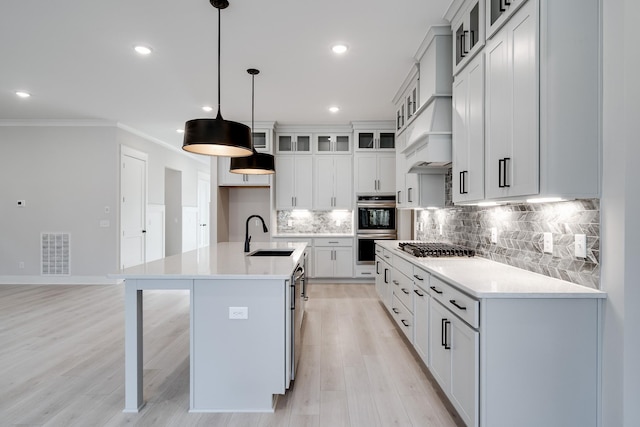 7233 Richvale Dr W, Fairview, TN 37062 - kitchen featuring stainless steel appliances, light wood-style floors, a kitchen island with sink, tasteful backsplash, and ornamental molding
