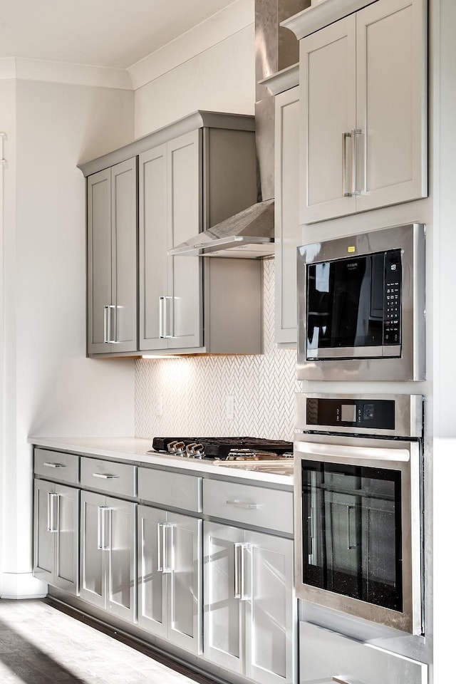 7262 Fairlawn Dr, Fairview, TN 37062 - kitchen featuring appliances with stainless steel finishes, ornamental molding, gray cabinetry, tasteful backsplash, and wall chimney range hood