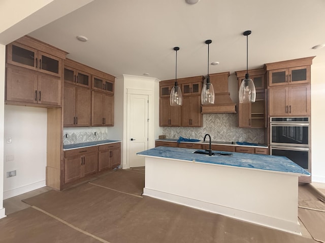 7262 Fairlawn Dr, Fairview, TN 37062 - kitchen featuring stainless steel double oven, backsplash, hanging light fixtures, brown cabinets, and a center island with sink