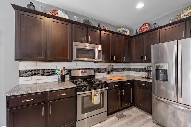 1301 Drury Ln, Mount Juliet, TN 37122 - kitchen featuring appliances with stainless steel finishes, light stone countertops, dark brown cabinetry, decorative backsplash, and light wood-style flooring