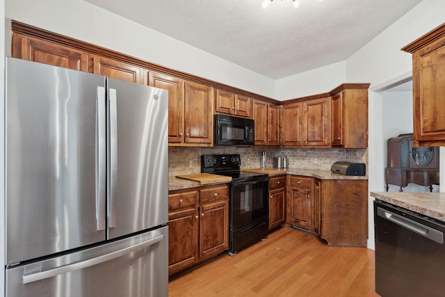 1908 Pointe Barton Dr, Lebanon, TN 37087 - kitchen with black appliances, light wood-style flooring, brown cabinetry, tasteful backsplash, and a textured ceiling