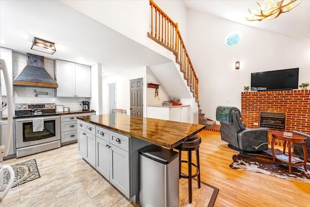 802 Evans Rd, Winchester, TN 37398 - kitchen with wall chimney exhaust hood, stainless steel range with electric stovetop, open floor plan, wood counters, and a breakfast bar area