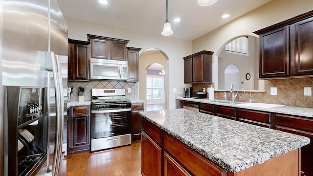 1007 Via Francesco Way, Spring Hill, TN 37174 - kitchen with stainless steel appliances, arched walkways, a center island, wood-type flooring, and decorative backsplash