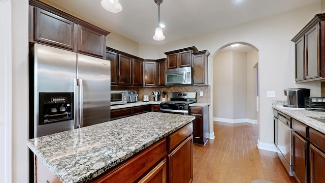 1007 Via Francesco Way, Spring Hill, TN 37174 - kitchen featuring appliances with stainless steel finishes, arched walkways, dark brown cabinets, decorative backsplash, and light stone counters