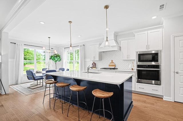 2636 Bramblewood Ln, Thompsons Station, TN 37179 - kitchen with stainless steel appliances, crown molding, light wood-style flooring, a kitchen island with sink, and white cabinetry