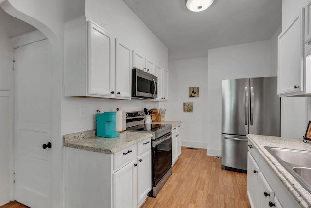 203 6th Ave, Columbia, TN 38401 - kitchen featuring stainless steel appliances, arched walkways, light wood finished floors, white cabinetry, and light stone counters