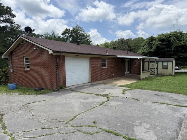 125 Benco Ln, Camden, TN 38320 - rear view of property featuring an attached garage, asphalt driveway, brick siding, a storage shed, and a lawn