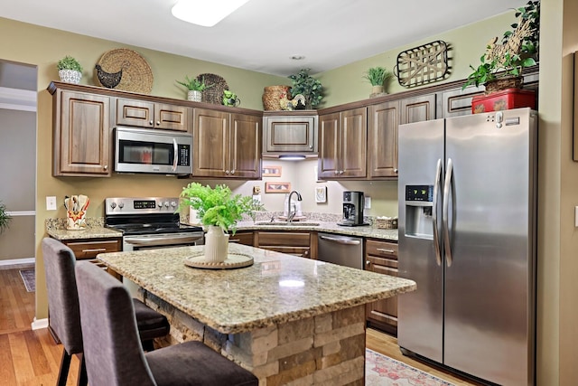 1511 Cardinal Ln, Mount Juliet, TN 37122 - kitchen featuring appliances with stainless steel finishes, light stone countertops, light wood finished floors, a center island, and a breakfast bar