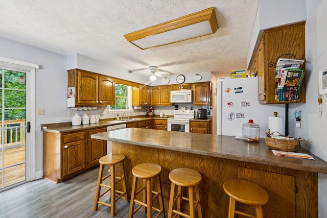 219 Lakeview Dr, Hohenwald, TN 38462 - kitchen featuring white appliances, a peninsula, a textured ceiling, brown cabinets, and light wood-type flooring