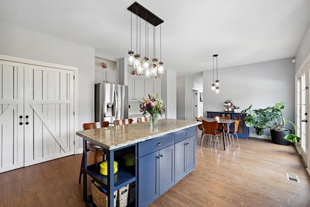 1209 Firth Ct, Franklin, TN 37067 - kitchen with stainless steel fridge, wood finished floors, pendant lighting, light stone countertops, and a kitchen island