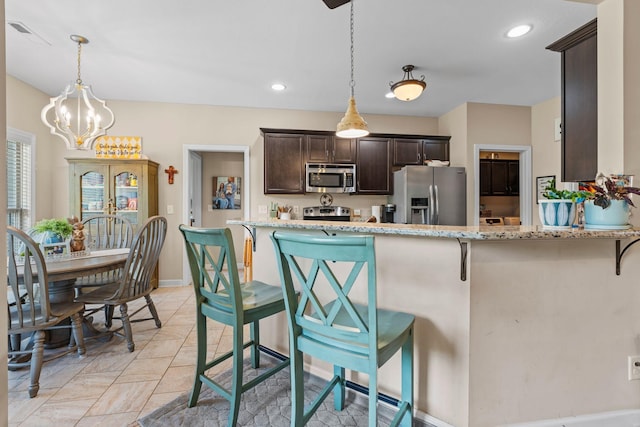 1372 Tidwell Switch Rd, Dickson, TN 37055 - kitchen featuring appliances with stainless steel finishes, dark brown cabinets, light stone countertops, a kitchen bar, and recessed lighting