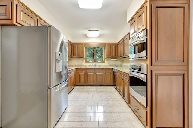 5122 Prince Phillip Cv, Brentwood, TN 37027 - kitchen featuring stainless steel appliances, brown cabinetry, tasteful backsplash, and light stone countertops