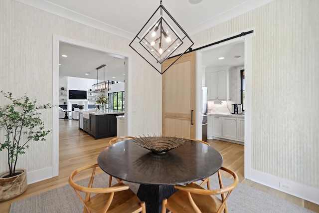 4720 Edwardian Trce, Franklin, TN 37067 - dining space with a barn door, wallpapered walls, light wood-style flooring, a chandelier, and crown molding