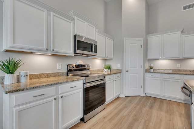 272 Thorpe Dr, Spring Hill, TN 37174 - kitchen with stainless steel appliances, white cabinets, light wood-style flooring, a high ceiling, and light stone counters