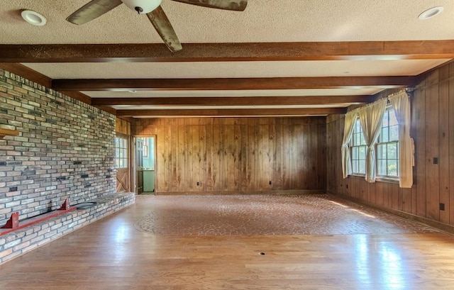 867 Lexington Hwy, Loretto, TN 38469 - unfurnished living room featuring beamed ceiling, wood finished floors, a textured ceiling, wood walls, and brick wall